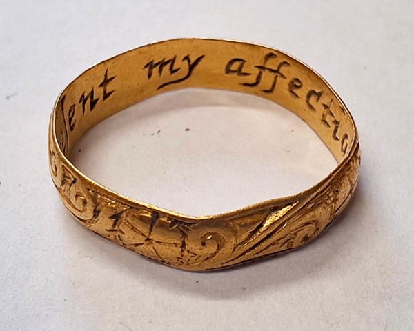 Photo of a gold ring with decorative scrollwork on the outside and an inscription running round the inside including the words 'my affection'. 